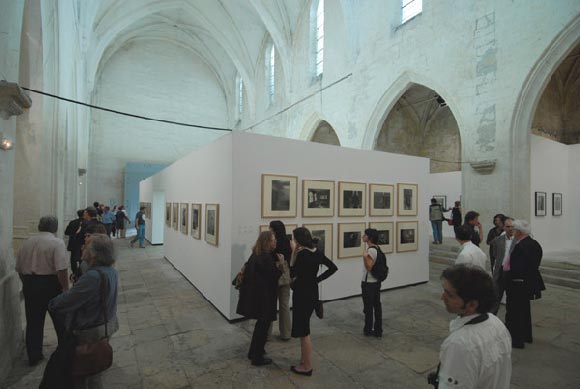 Imagen del lugar de la exposición con varios asistentes contemplando las fotografías o charlando alrededor de ellas