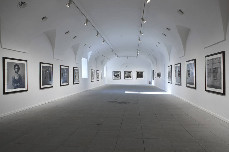 Una de las salas de la exposición; pueden verse cuadros de Alix con marco negro sobre paredes blancas. Focos en el techo y un par de ventanas por donde entra luz natural.